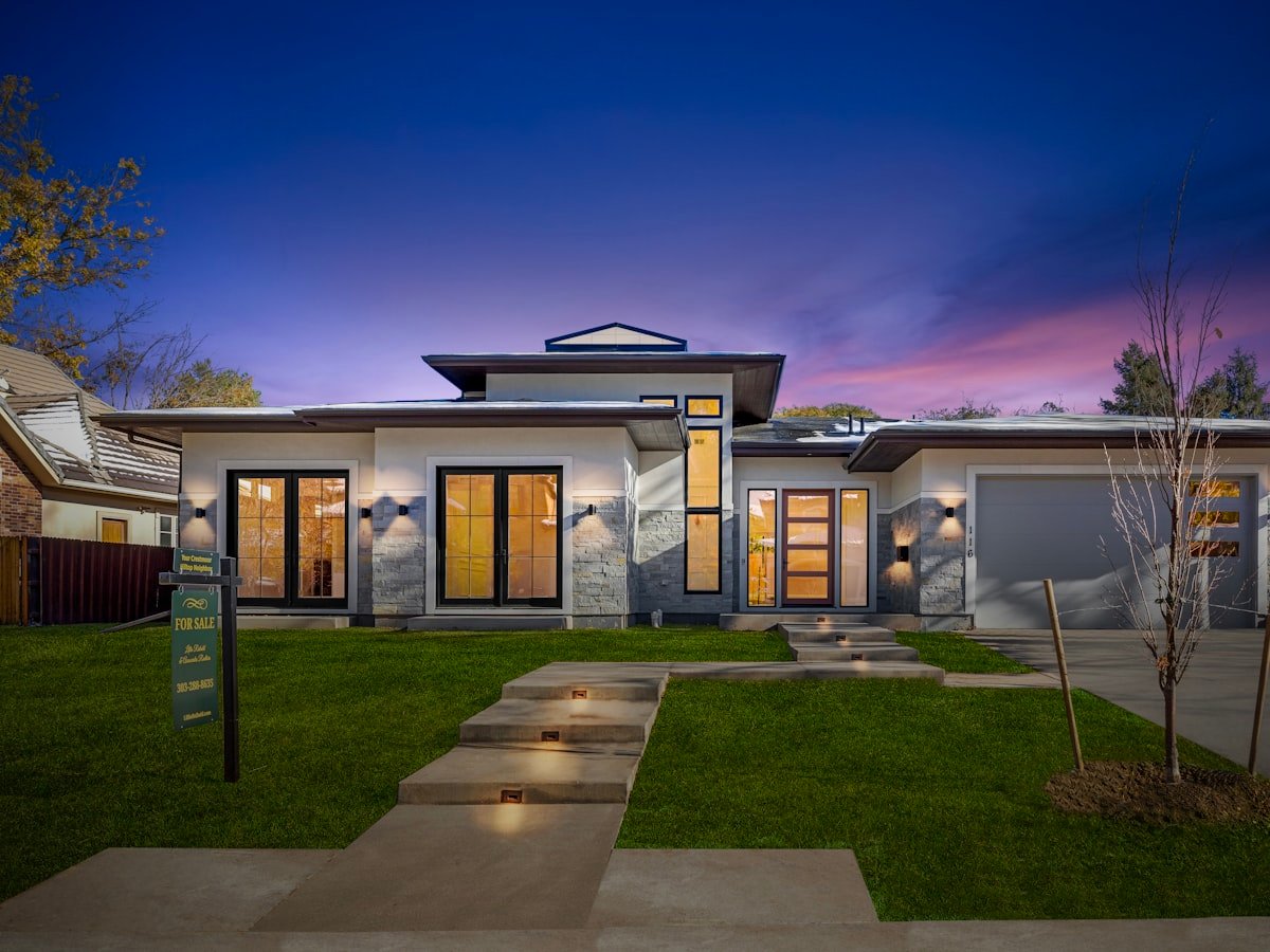 A prairie-style home at dusk with warm interior lighting, deep eaves and stone detailing.