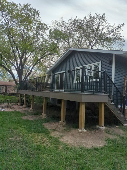 Elevated timber deck with black metal railing attached to a grey house.