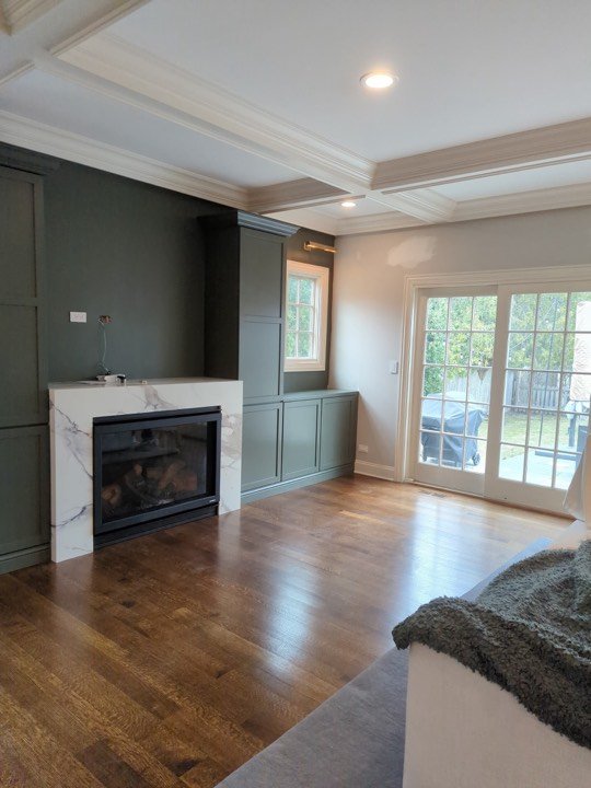 Great room with a coffered ceiling, fireplace surround and built-in cabinetry.
